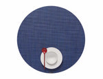 A white bowl and plate with a red spoon sit together on a large, round, textured blue Mini Basketweave Round Placemat—ideal for adding color to any dining occasion.