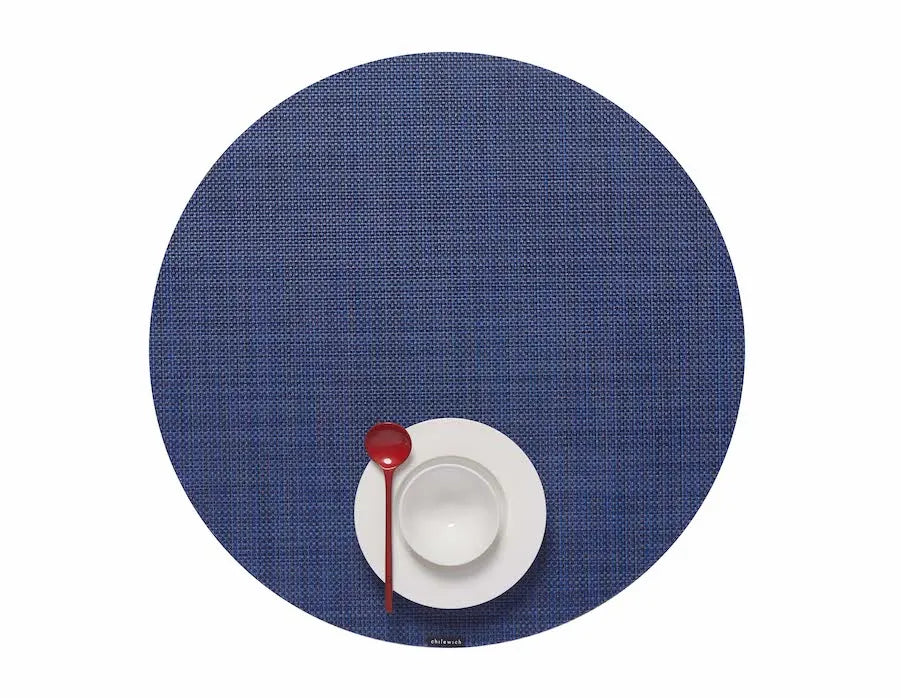 A white bowl and plate with a red spoon sit together on a large, round, textured blue Mini Basketweave Round Placemat—ideal for adding color to any dining occasion.