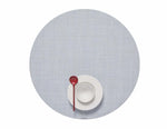 A white bowl and plate with a red spoon sit atop the Mini Basketweave Round Placemat in light gray, viewed from above—a stylish touch for any dining occasion.
