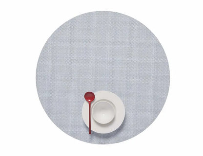 A white bowl and plate with a red spoon sit atop the Mini Basketweave Round Placemat in light gray, viewed from above—a stylish touch for any dining occasion.