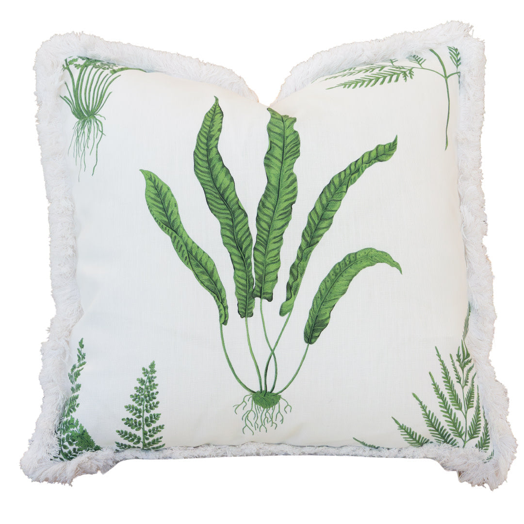 The Woodland Fern Outdoor Pillow is a square white pillow adorned with green botanical fern designs and finished with white fringe along the edges, featuring a hidden zipper closure for easy removal.