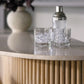Two glasses with ice cubes and a cocktail shaker rest on the light wood Anton Bar, which features clever storage solutions and is accented by a vase in the background.
