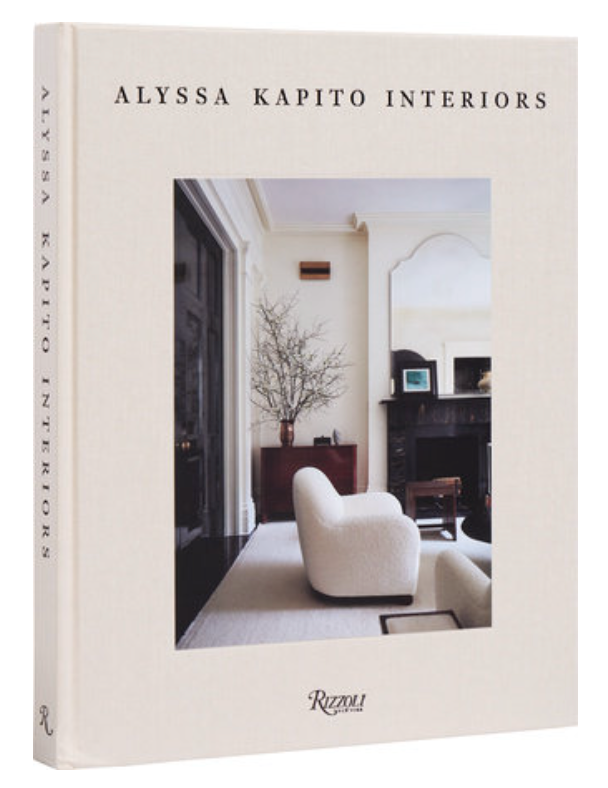 Alyssa Kapito: Interiors featuring a minimalist living room with white armchair and neutral tones on the cover, enhanced by luxurious textures. Rizzoli logo at the bottom.