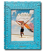 Cover of the book "Zanzibar" featuring a man on a beach holding a colorful cloth against a blue sky background. The cover is framed with intricate blue patterns and text, evoking the essence of Zanzibar and its rich Swahili rituals.