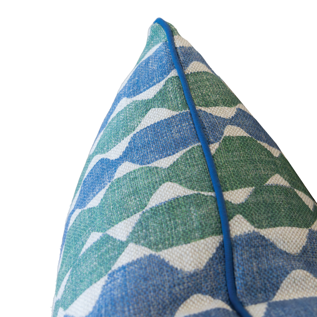 Close-up of the Whittle Blue Green Lumbar Pillow corner, showcasing vibrant blue and green wavy patterns with a refined blue piping edge, set against a white background. This custom pillow also features a hidden zipper closure for a seamless finish.