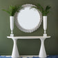 A white Kasper Demilune Console Table sits against an olive green wall, topped with two tall vases of palm leaves, while a round scalloped mirror and a blue wave-patterned rug complete the stylish entryway.