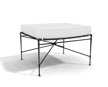 The Amalfi Ottoman has a minimalist design, featuring a white cushion on a black hand-forged steel frame with slender legs and crossbar supports.