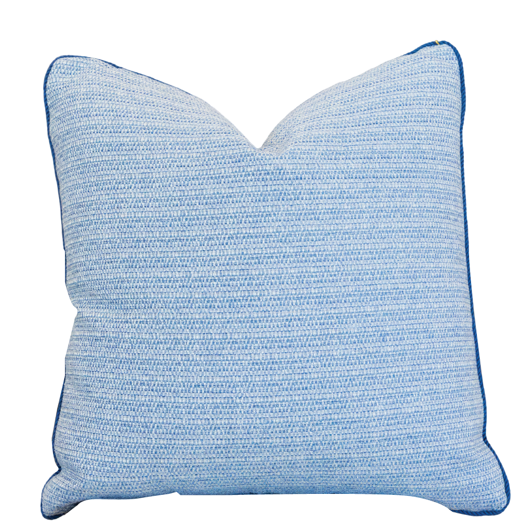 The Roxam Blue Pillow is a square, light blue woven pillow with subtle horizontal stripes and dark blue piped edges. It features a hidden zipper closure for a seamless look and is showcased against a white background.