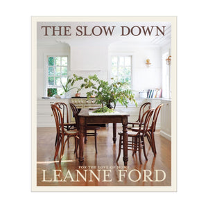 The cover of "The Slow Down" features a wooden dining table and chairs in a bright white kitchen, capturing Leanne Ford's signature interior design style.