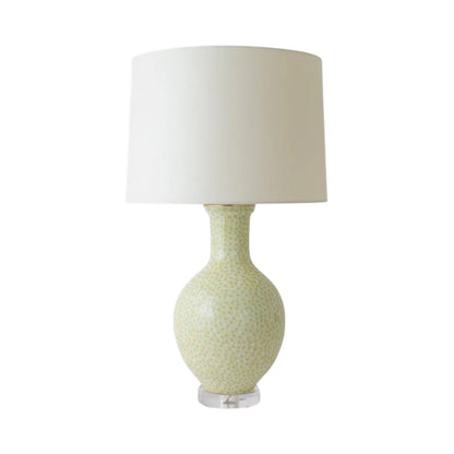 The Presidio Lamp in Dappled Green is a handcrafted ceramic lamp with a patterned base, pale green glaze, large white cylindrical shade, and clear round base.