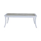The Bermuda Coffee Table features a rectangular design with a light wood top and white, slightly curved legs for an elegant outdoor look.